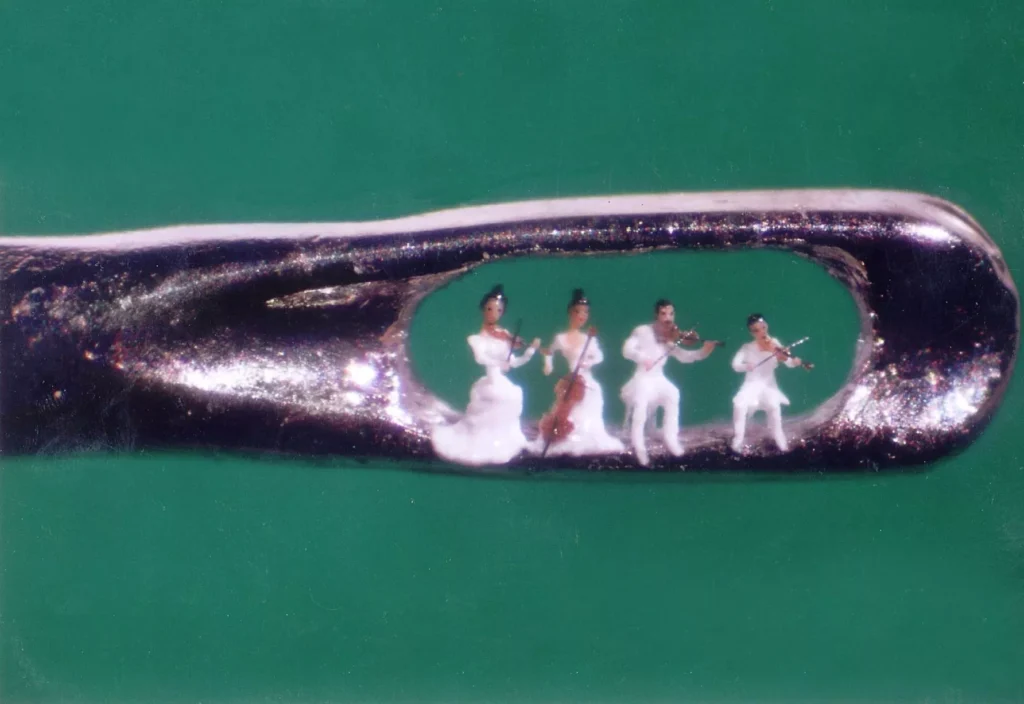 Micro-sculpture by Willard Wigan depicting a string quartet performing inside the eye of a sewing needle, with four miniature musicians dressed in white.
